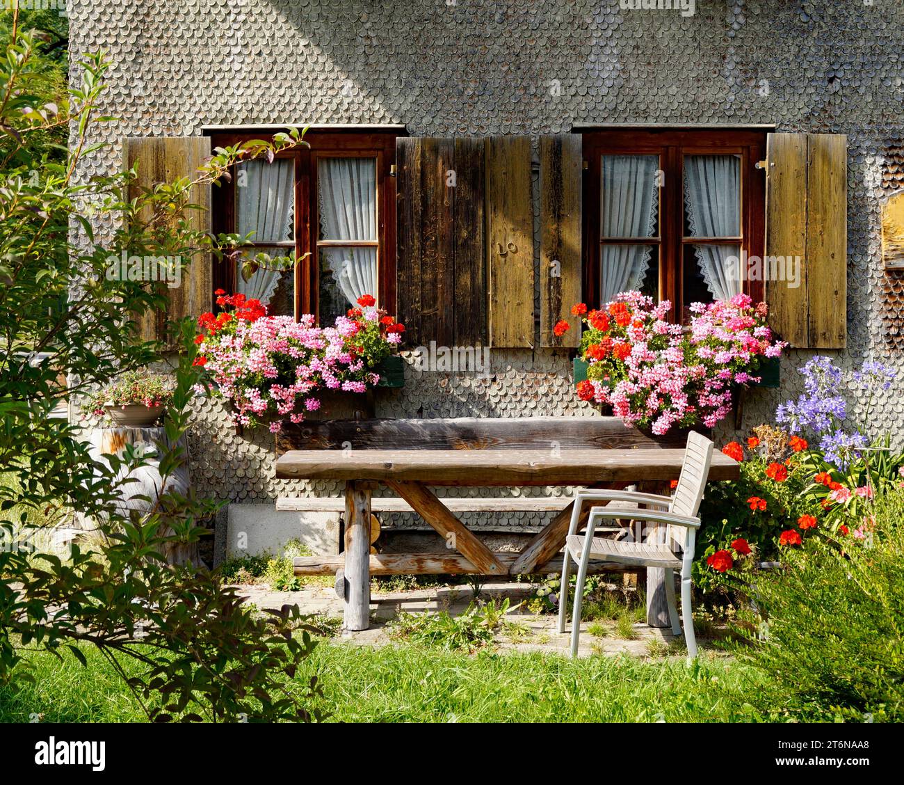 Tradizionale casa di campagna alpina bavarese ricoperta di ciottoli di legno con gerani su una sporgenza della finestra nelle Alpi bavaresi il giorno di settembre a Unterjoch Foto Stock