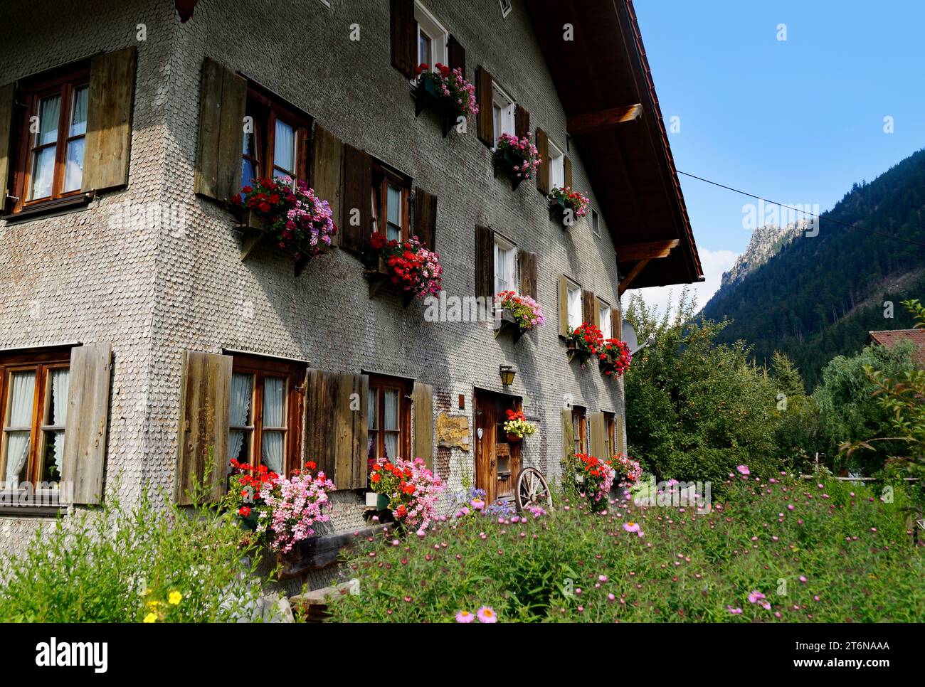 Tradizionale casa di campagna alpina bavarese ricoperta di ciottoli di legno con gerani su una sporgenza della finestra nelle Alpi bavaresi il giorno di settembre a Unterjoch Foto Stock