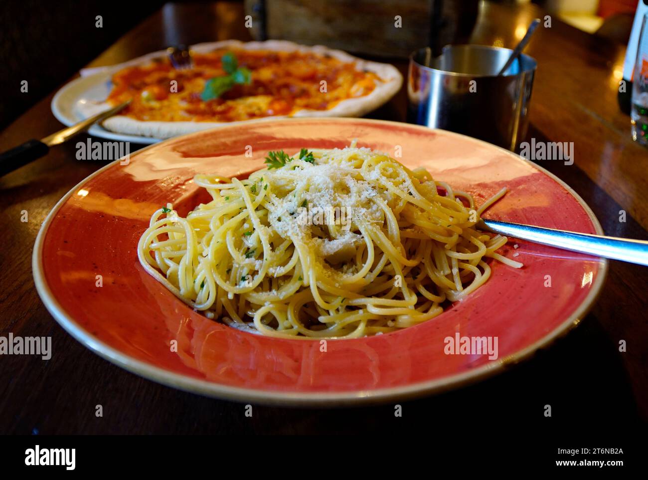 Un grande piatto rosso di deliziosi spaghetti caldi aglio e olio cosparso di parmigiano in un tradizionale ristorante italiano di Ulma, Germania Foto Stock