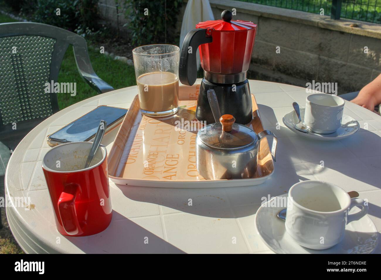la famiglia sta bevendo un caffè in giardino e c'è un telefono cellulare sul tavolo Foto Stock