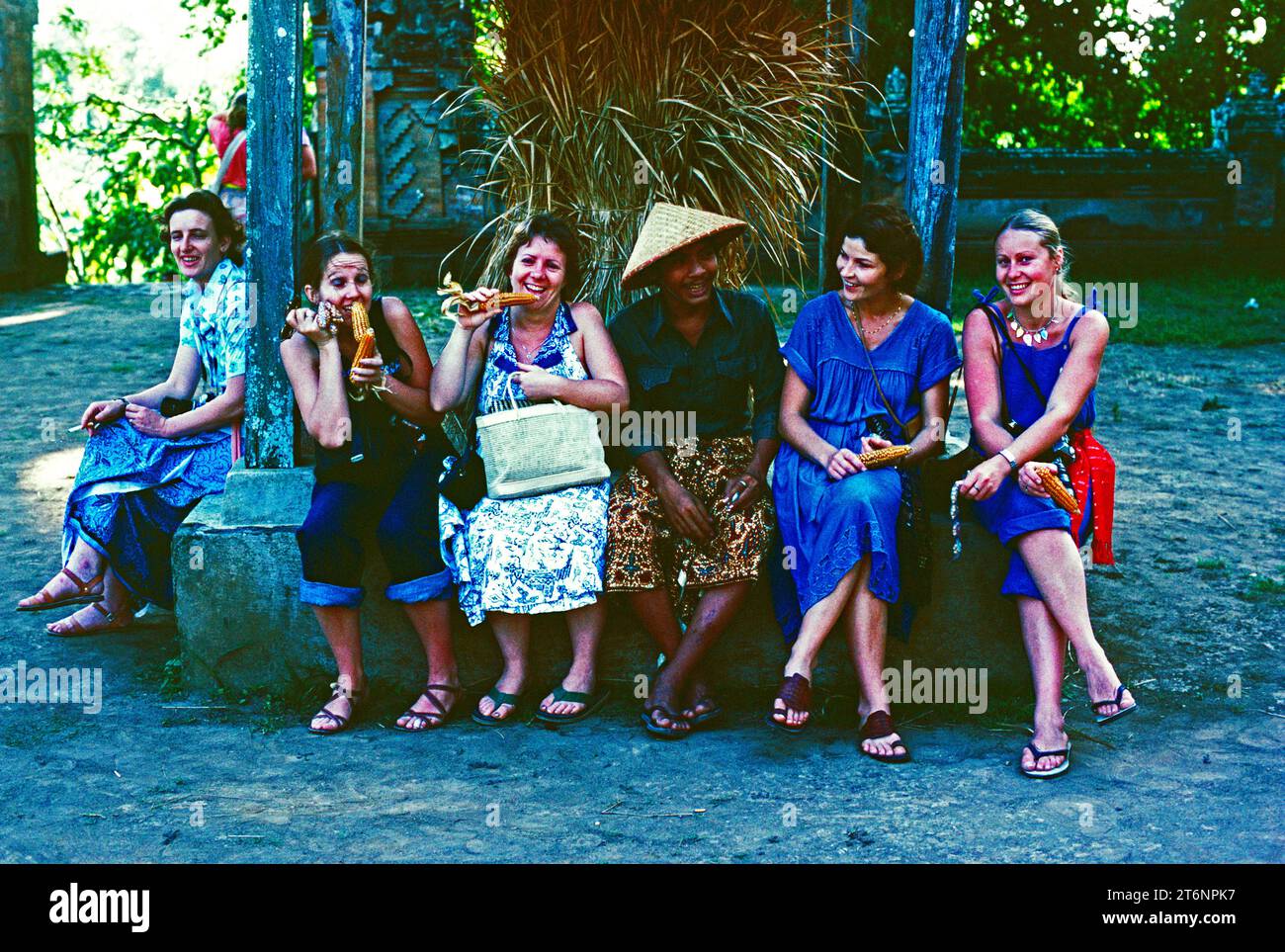 Indonesia. Bali. Turisti con un uomo del posto seduto all'aperto sotto gli alberi. Foto Stock
