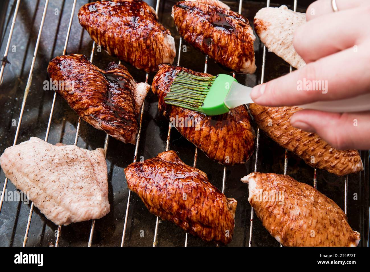 Avvicinare la mano della persona applicando ali di pollo arrostite con olio e spazzolina Foto Stock Avvicinare la mano della persona applicando ali di pollo arrostite con olio e spazzolina Foto Stock