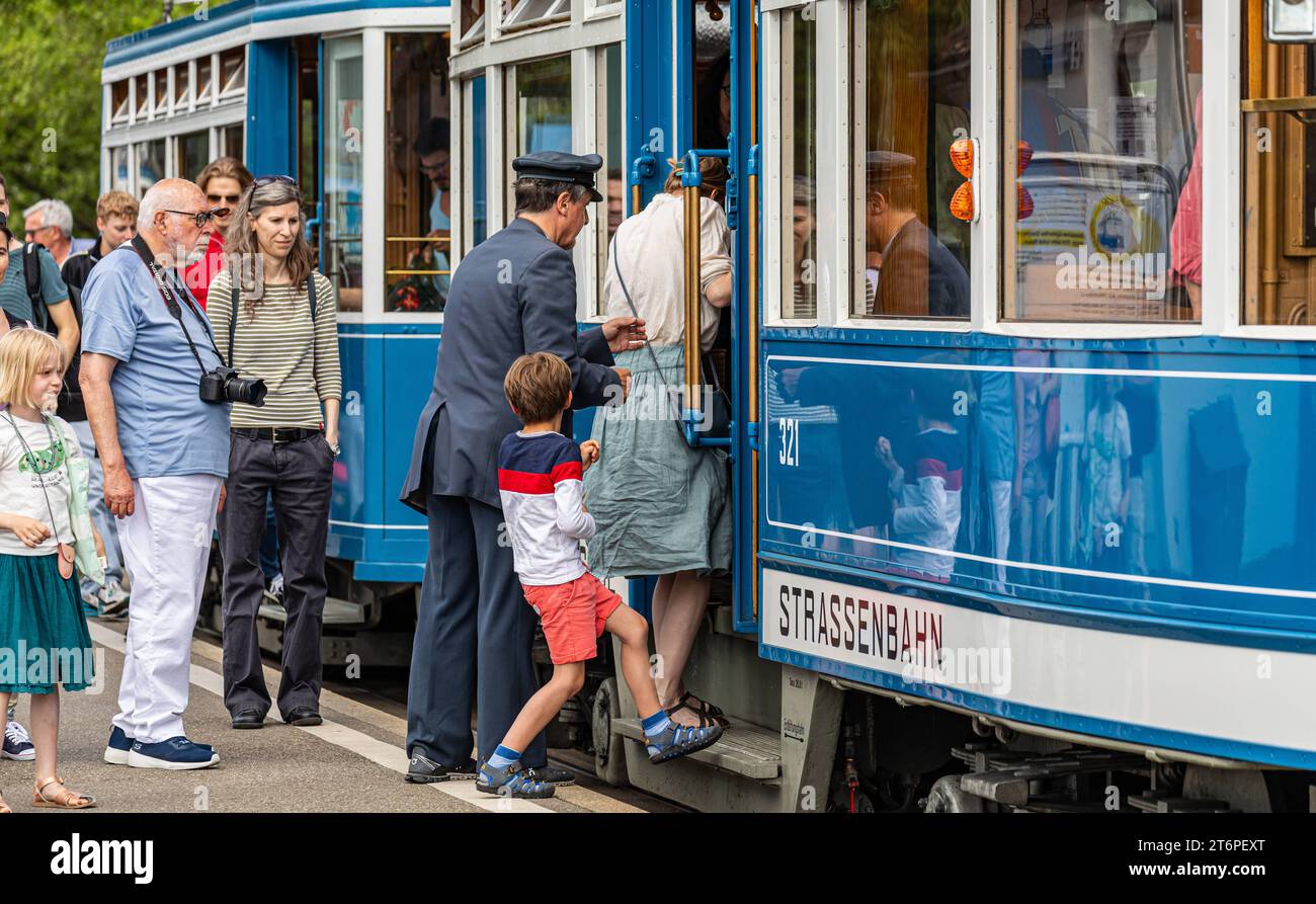 DAS Zürcher tram - Elefant Ein Kontrolleur hilft den Passagieren ins tram einzusteigen. 1930 als das tram unter dem Übername Elefant an die Städtische Strassenbahn Zürich ausgeliefert wurde, la guerra muore üblich. Hier steht das tram im Einsatz beim Jubiläumsanlass 175 Jahre Eisenbahn Schweiz. Zürich, Schweiz, 21.05.2022 *** il tram Zurich Elefant un ispettore aiuta i passeggeri a salire a bordo del tram nel 1930, quando il tram è stato consegnato alla funivia municipale di Zurigo con il soprannome di Elefant, questa era pratica comune qui il tram è in uso in occasione del 175° anniversario della SWI Foto Stock