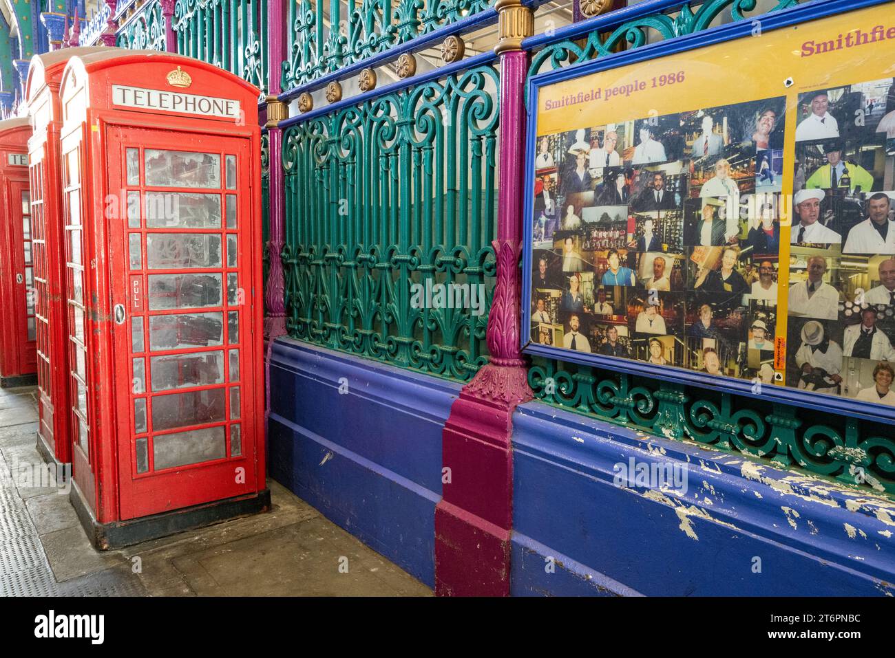 Le tradizionali cabine telefoniche rosse di Londra sono visibili fuori dalle colorate ringhiere di Smithfield Market con un poster che mostra i volti dei commercianti Foto Stock