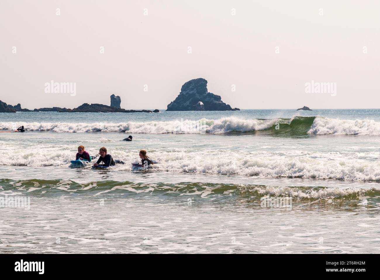 Tre giovani studenti di surf cavalcano un'onda all'Ecola State Park, Oregon Foto Stock