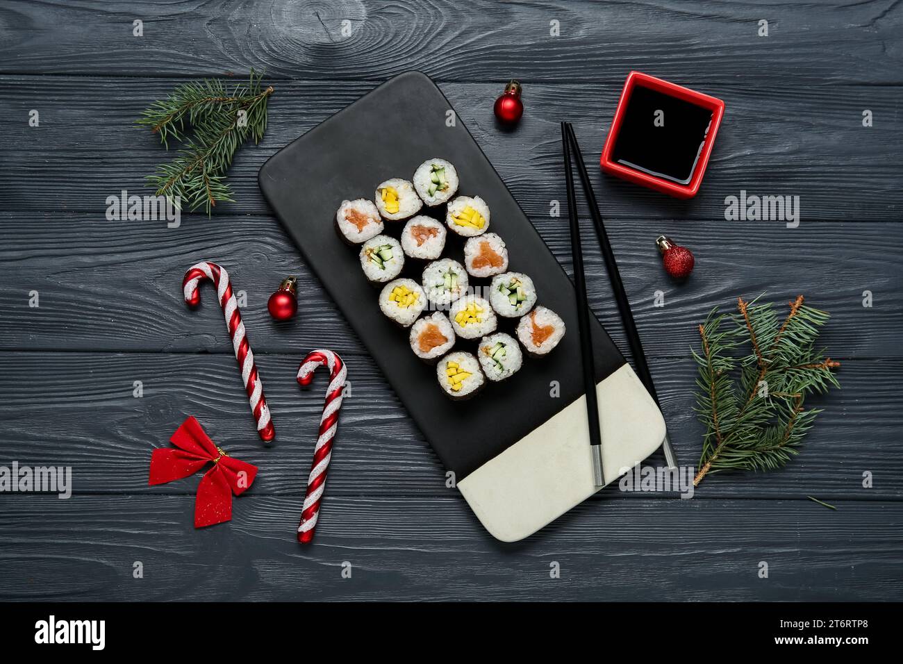 Tavola di gustosi panini sushi con rami di abete e decorazioni natalizie su sfondo di legno nero Foto Stock
