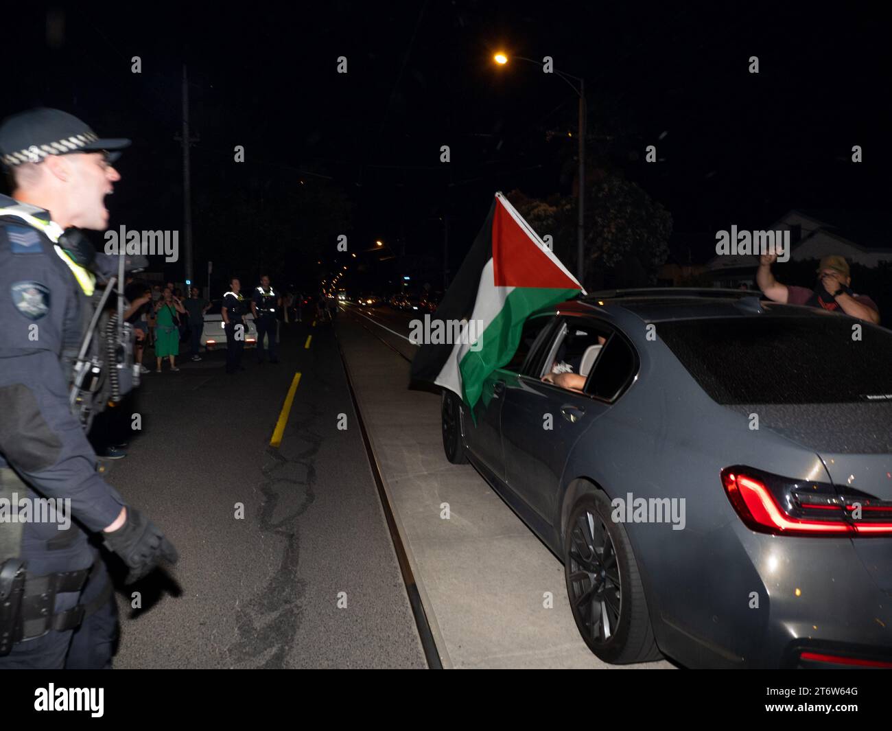 Un agente di polizia grida a un autista di spostare la sua auto con una bandiera palestina mentre si ferma sulla strada di fronte ai contrautori pro-Israele dopo che una catena di ristoranti Burgertory di proprietà di Hesham Tayah palestinese-australiano è bruciata durante la notte nel sobborgo più ebraico di Melbourne, i manifestanti pro-Palestina si sono riuniti in un parco vicino dove si sono verificati violenti scambi con contromanifestanti pro-israeliani. La polizia ha distribuito spray al pepe su entrambi i lati e ha fatto un arresto. Foto Stock