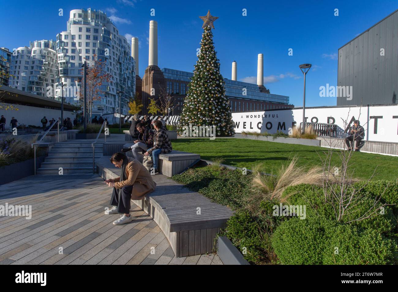 Persone sedute di fronte alla centrale elettrica di Battersea con Prospect Place appartamenti residenziali di lusso sullo sfondo. Londra , Regno Unito. Foto Stock