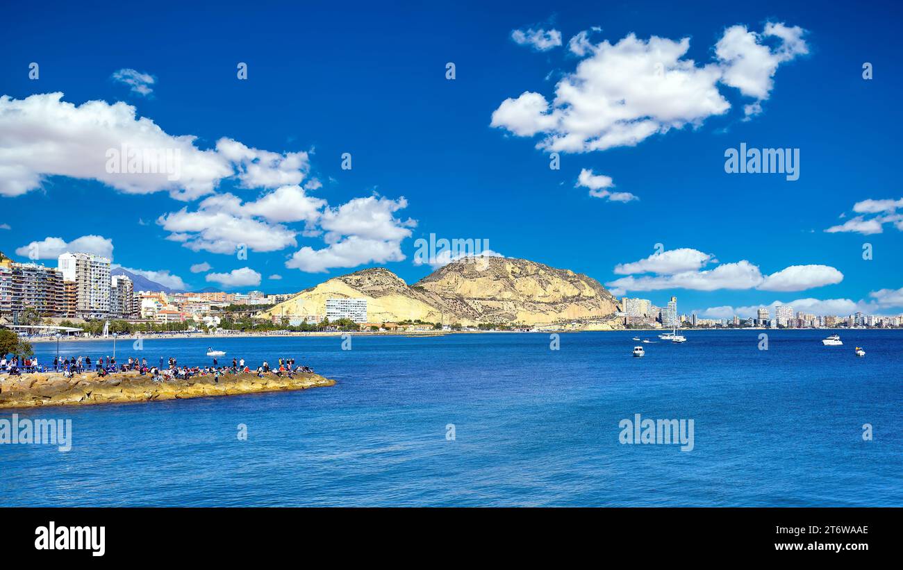 Alicante, Spagna, gente sulla costa che guarda la linea di partenza della Ocean Race. Colline e parte del paesaggio urbano sullo sfondo. Foto Stock