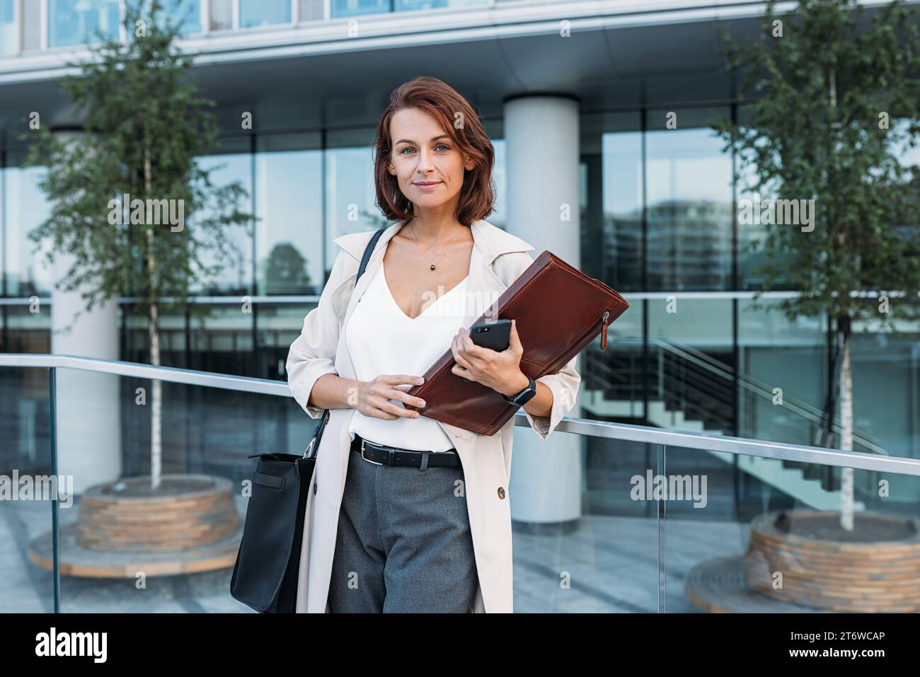 Donna sicura di mezza età che tiene una cartella contro il business building Foto Stock
