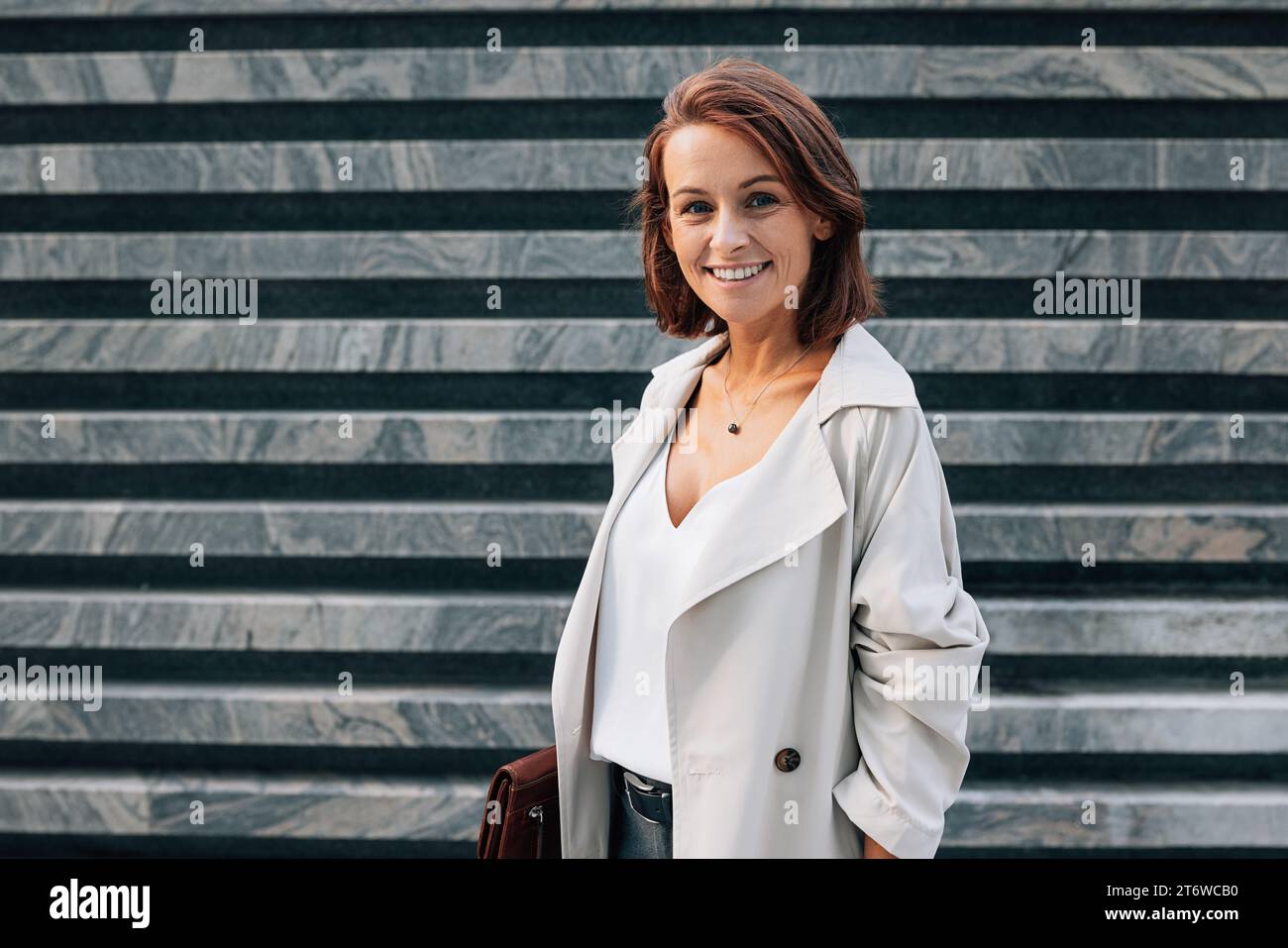 Ritratto di una donna sorridente di mezza età con peli di zenzero che guarda la fotocamera mentre si trova all'aperto Foto Stock