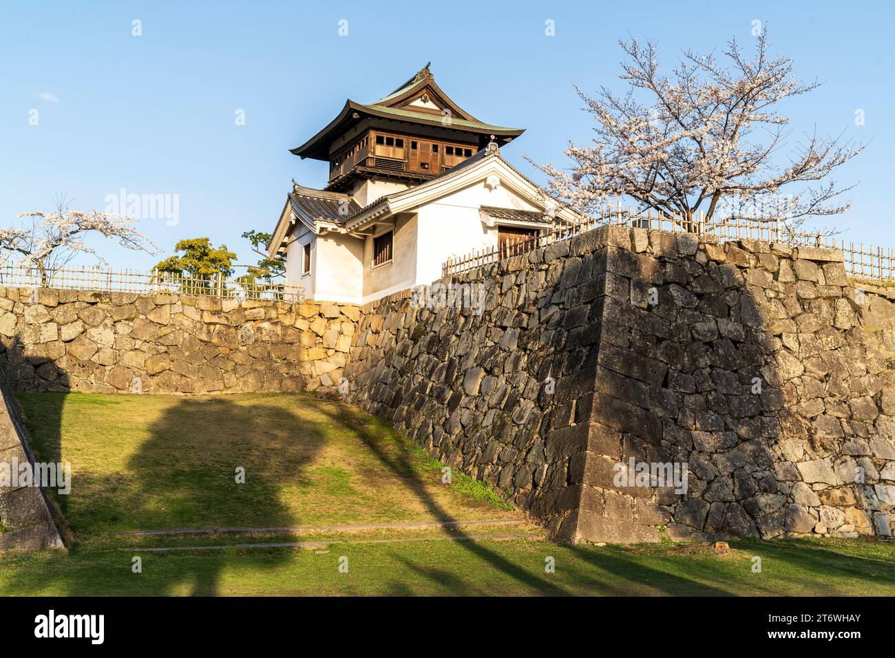 Castello di Fukuyama in Giappone. Shorou, torretta con campana, un importante patrimonio culturale, con la difesa del muro di pietra di ishigaki e alberi di ciliegio in fiore. Cielo blu Foto Stock