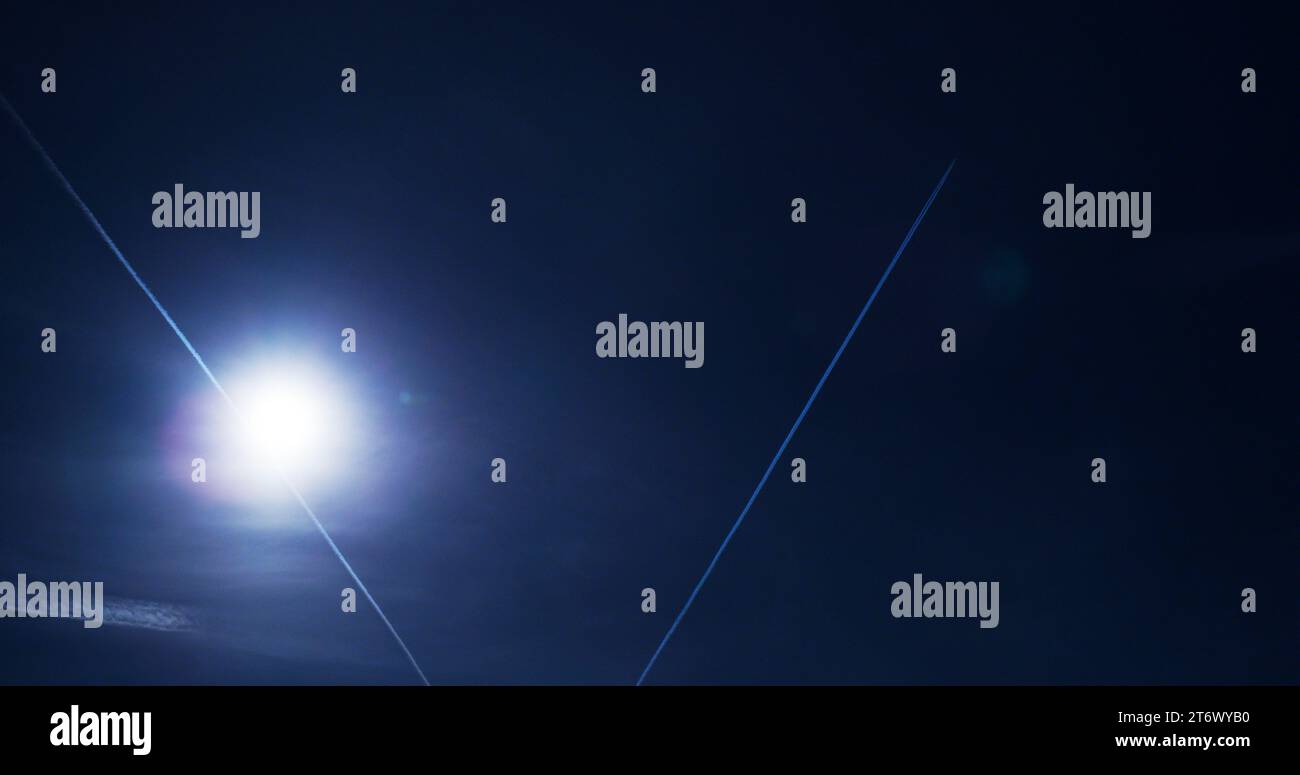 Sentieri di condensazione, maestosi e fugaci, fluttuano delicatamente sotto un sole ardente in un cielo blu profondo. Foto Stock