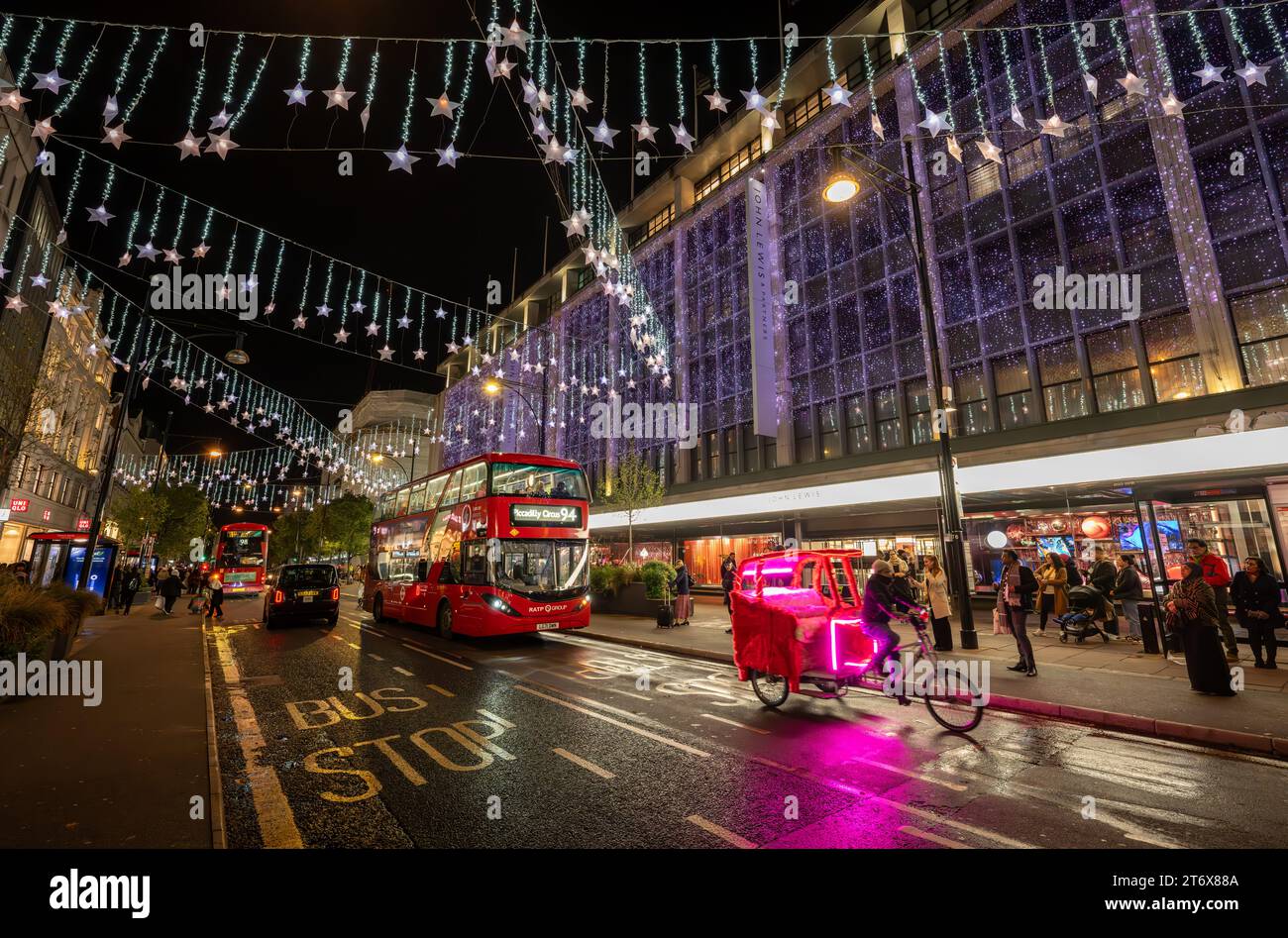 Londra, Regno Unito: Oxford Street, una famosa via dello shopping di Londra con le luci natalizie. Un pedicab e un autobus sono fuori dal grande magazzino John Lewis. Foto Stock