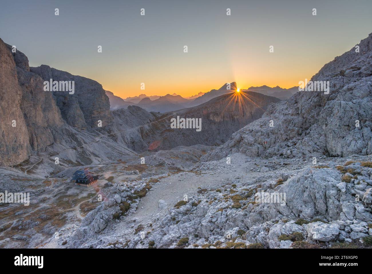 Il sole sorge dietro la montagna della Marmolada, i raggi del sole illuminano la valle alpina con la capanna Antermoia CAI. Alba in montagna. Foto Stock