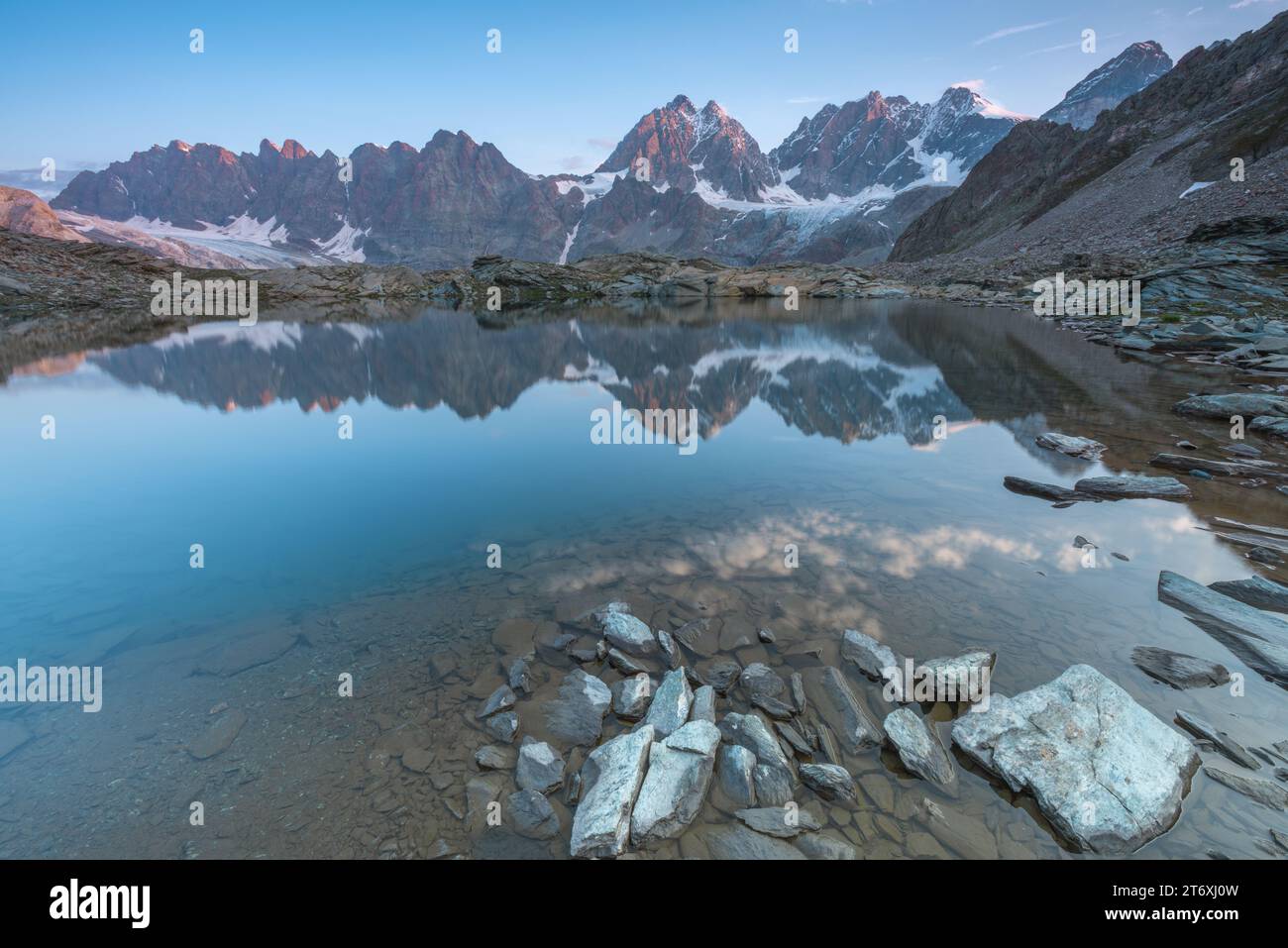 Alba alpina con cielo mattutino che si riflette in un piccolo lago perfettamente fermo. Lago Forbici vicino al Piz Bernina nelle Alpi italiane. Foto Stock