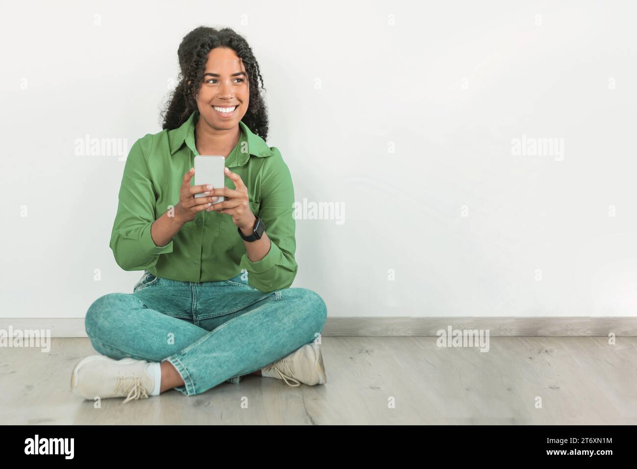 Signora nera che sorride mentre invia messaggi al cellulare in casa Foto Stock