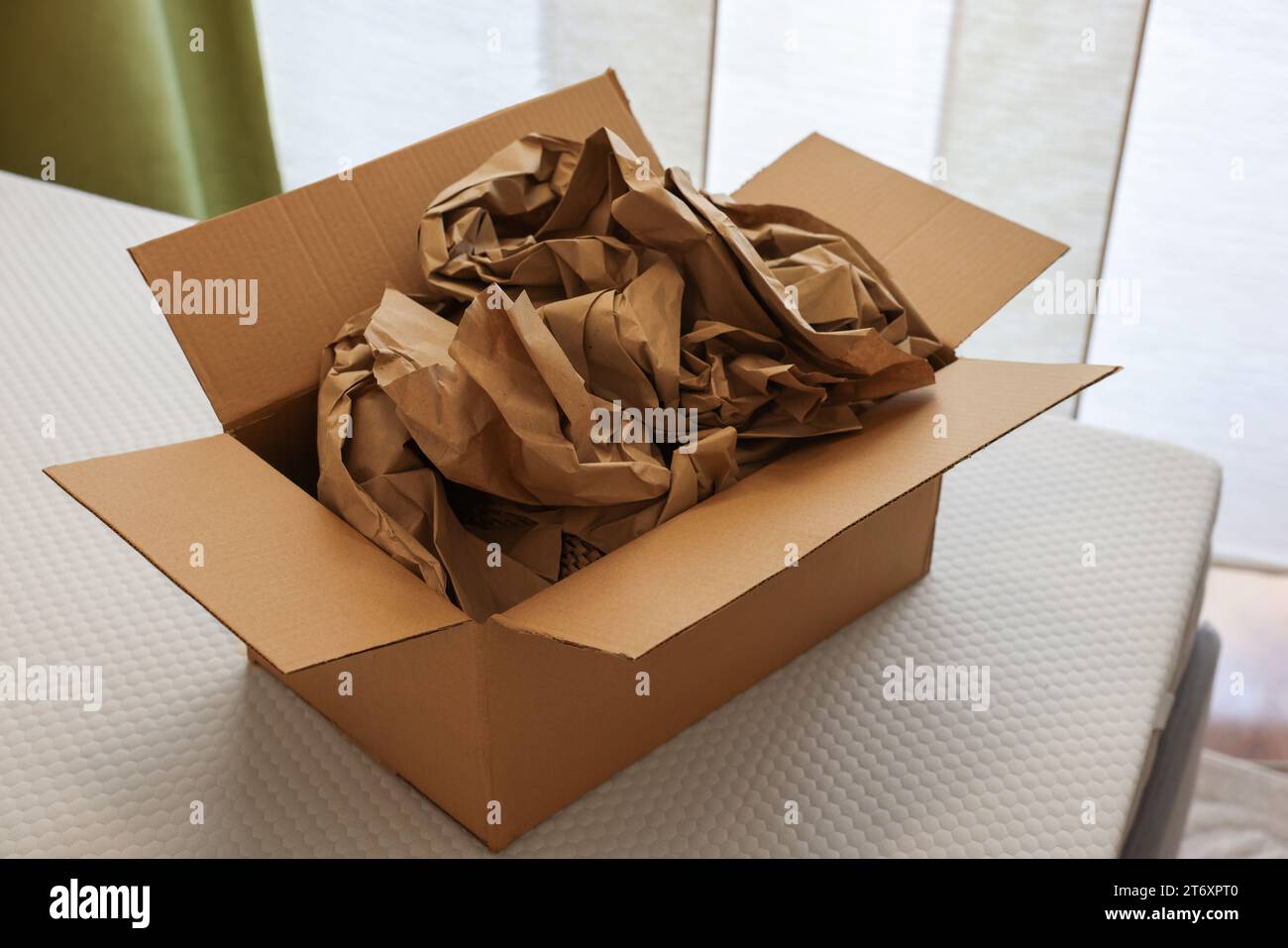 Scatola di cartone aperta con stucco di carta marrone schiacciata su materasso bianco per interni Foto Stock