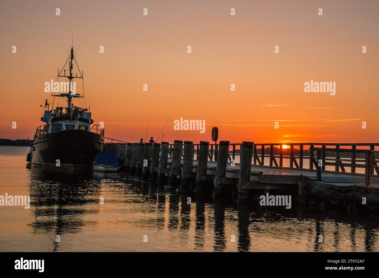 Tramonto marittimo. La nave è ancorata al molo. Riflessi delle tavole di legno sull'acqua Foto Stock