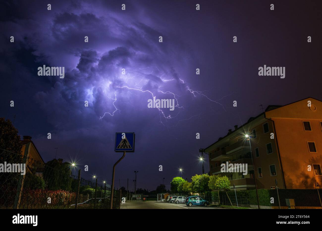 Più fulmini si diramano dall'imponente thunderhead che sovrasta condomini e case della città. Tempesta estiva con fulmini ramificati. Foto Stock