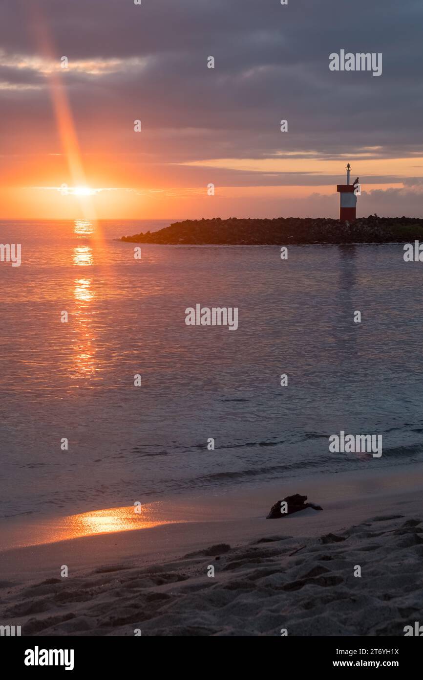 Vista del faro di Punta Carola e della spiaggia durante un tramonto rossastro, dell'isola di San Cristobal e dell'arcipelago delle Galapagos Foto Stock