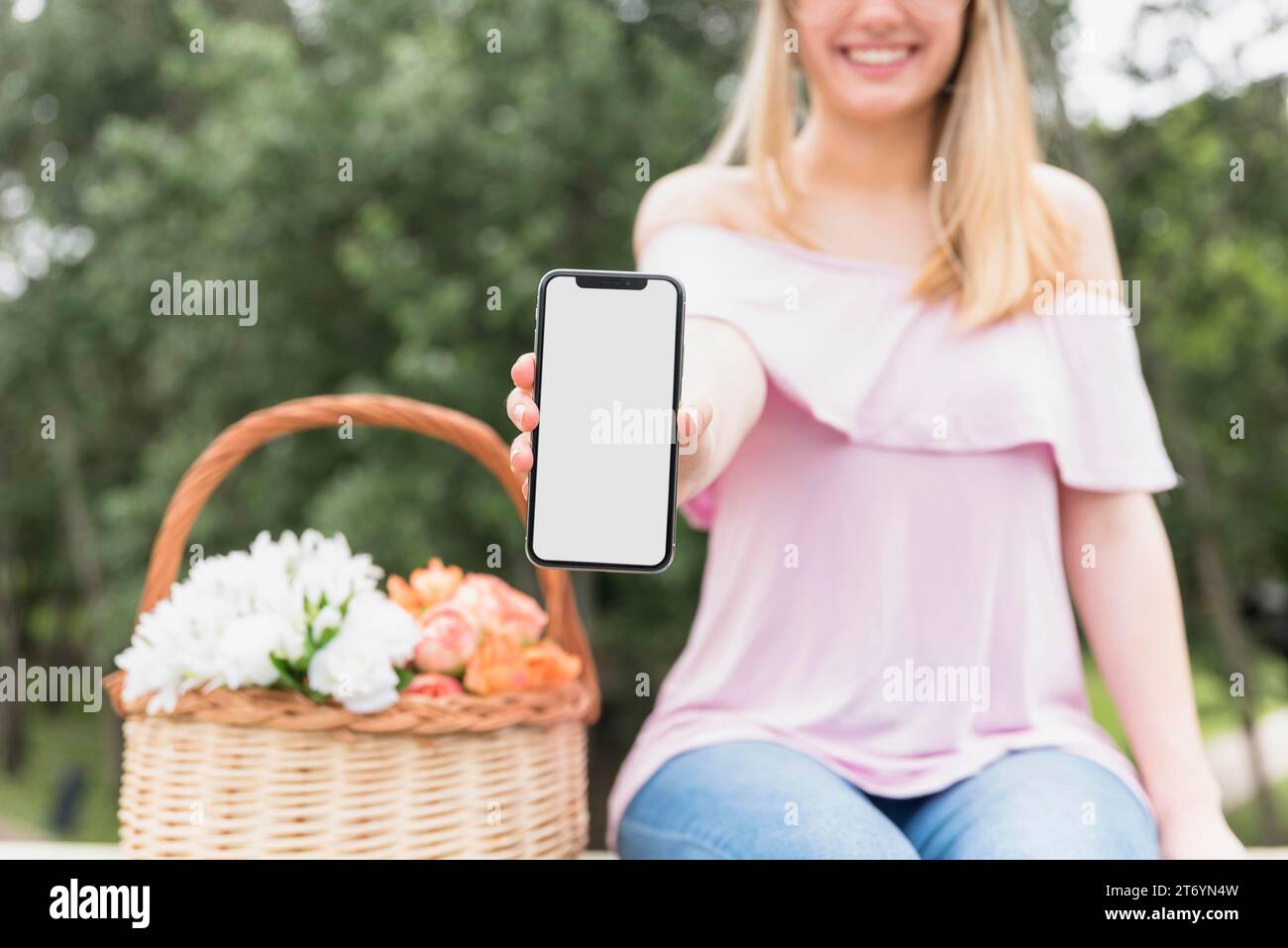 Signora sorridente che mostra il telefono cellulare vicino alla fioritura Foto Stock