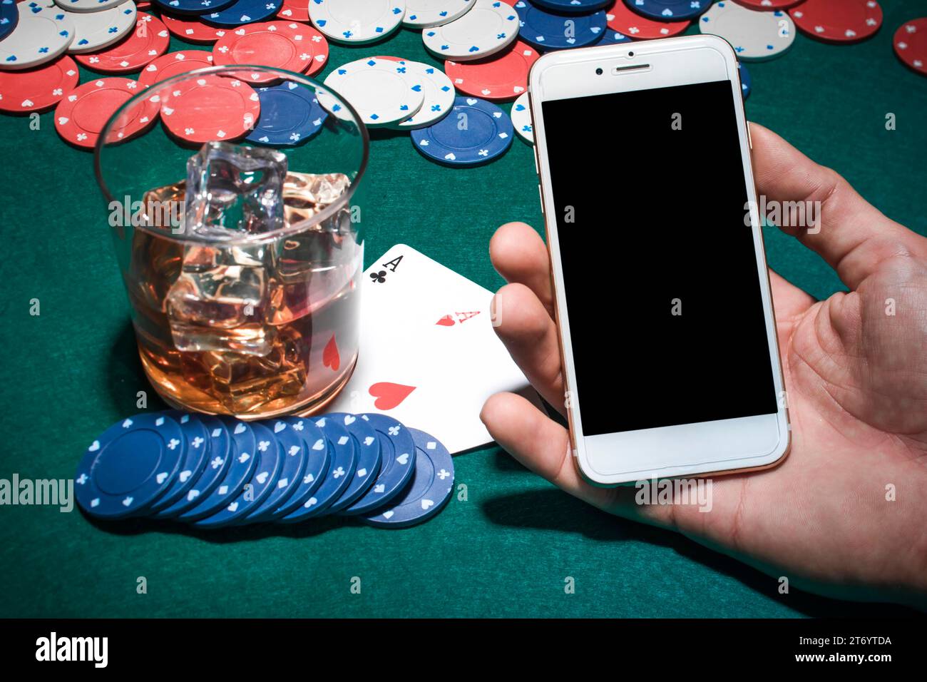 Mano dell'uomo che tiene il tavolo da poker del cellulare con bicchiere di whisky Foto Stock