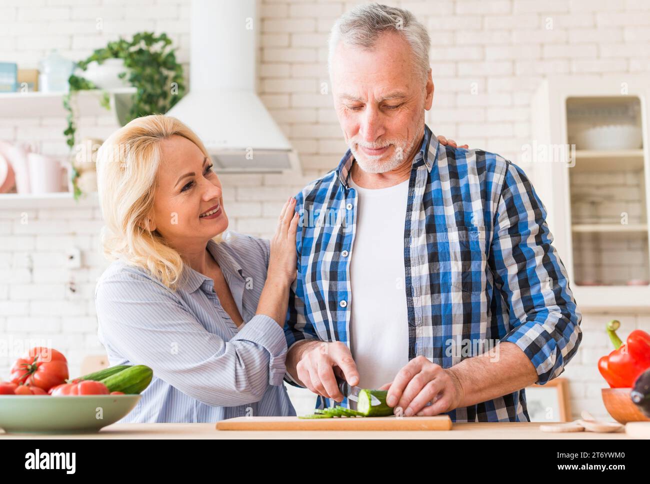 Donna sorridente che sostiene il marito che taglia il cetriolo con la cucina da tavolo dei coltelli Foto Stock
