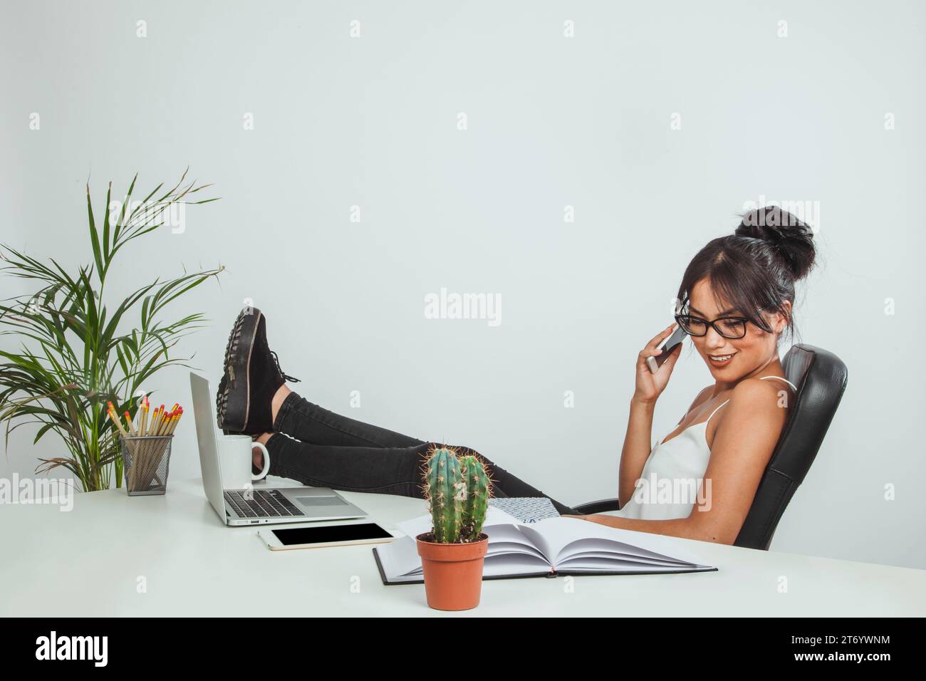 Smiley Woman con i piedi della scrivania che parla con il telefono Foto Stock