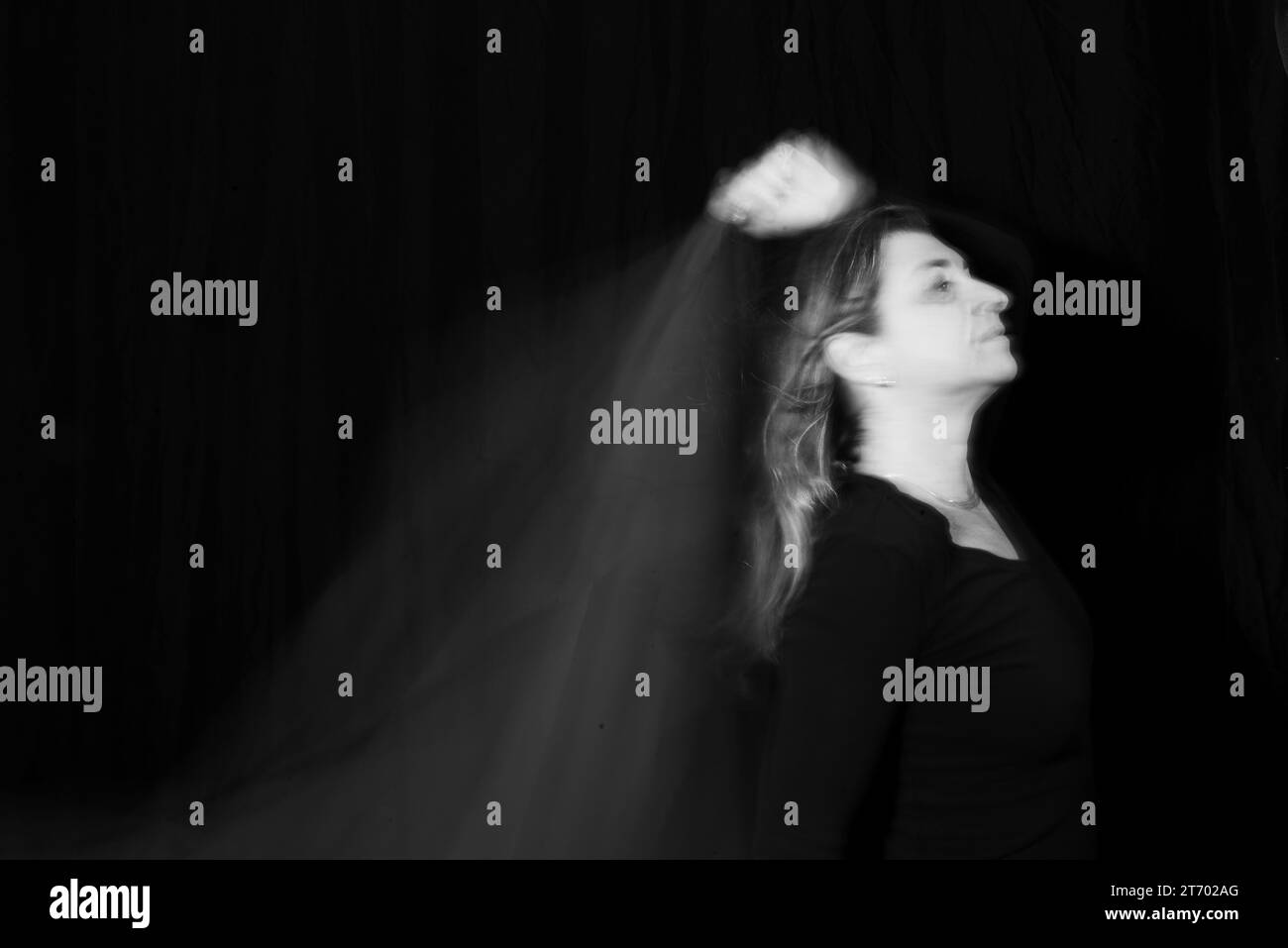 Foto in bianco e nero di una donna che si esibisce in performance astratte con movimenti sfocati. Sfondo scuro. Foto Stock