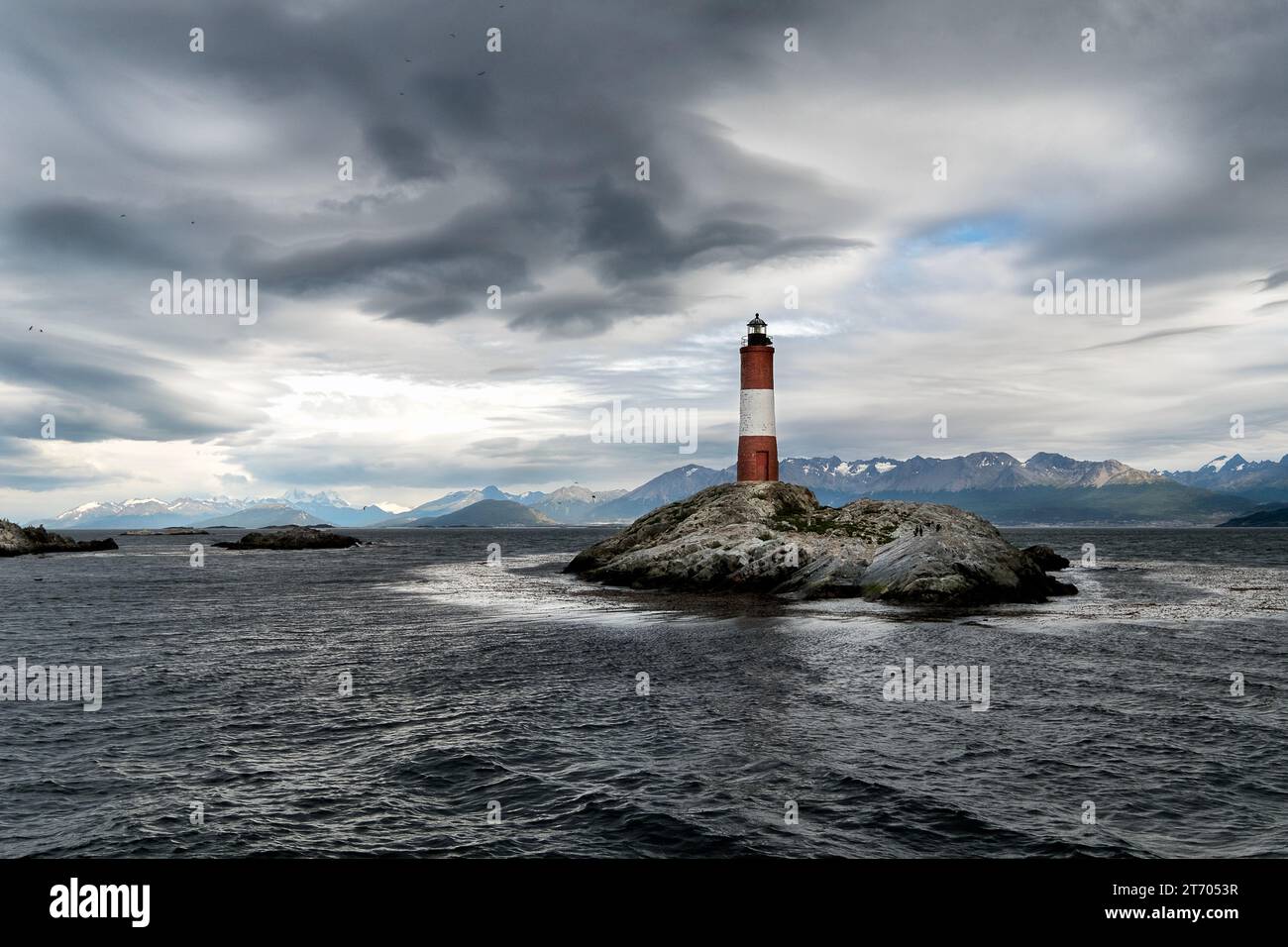 Vista panoramica dell'isola rocciosa dove si trova il faro di Les Eclaireurs, sotto un cielo nuvoloso e le montagne sullo sfondo. Ushuaia, ti Foto Stock