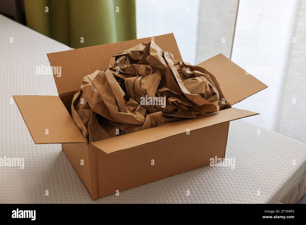 Scatola di cartone aperta con stucco di carta marrone schiacciata su materasso bianco per interni Foto Stock