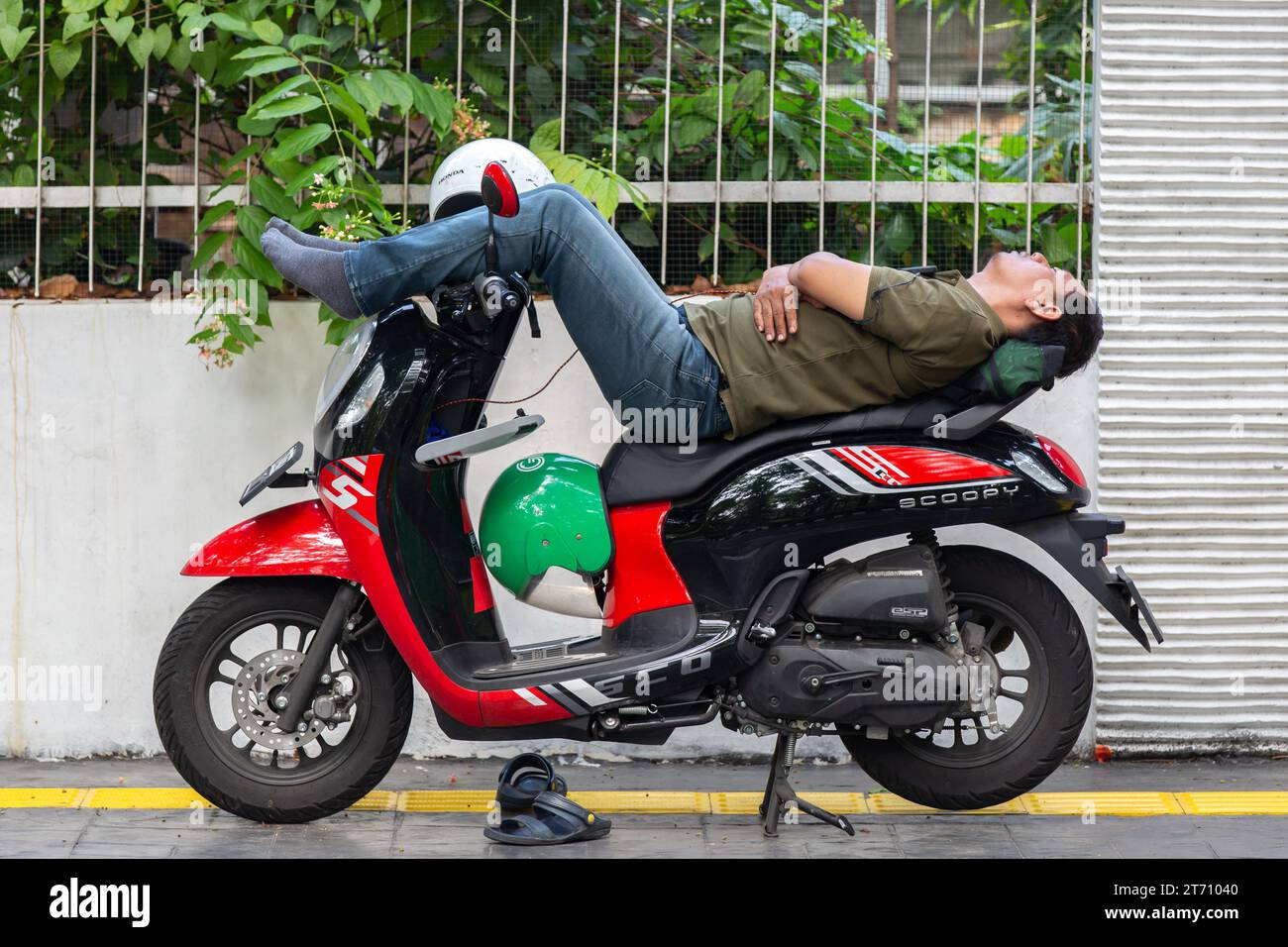 Giacarta, Indonesia - 11 novembre 2023: Un uomo non identificato che dorme sullo scooter parcheggiato sul marciapiede. Foto Stock