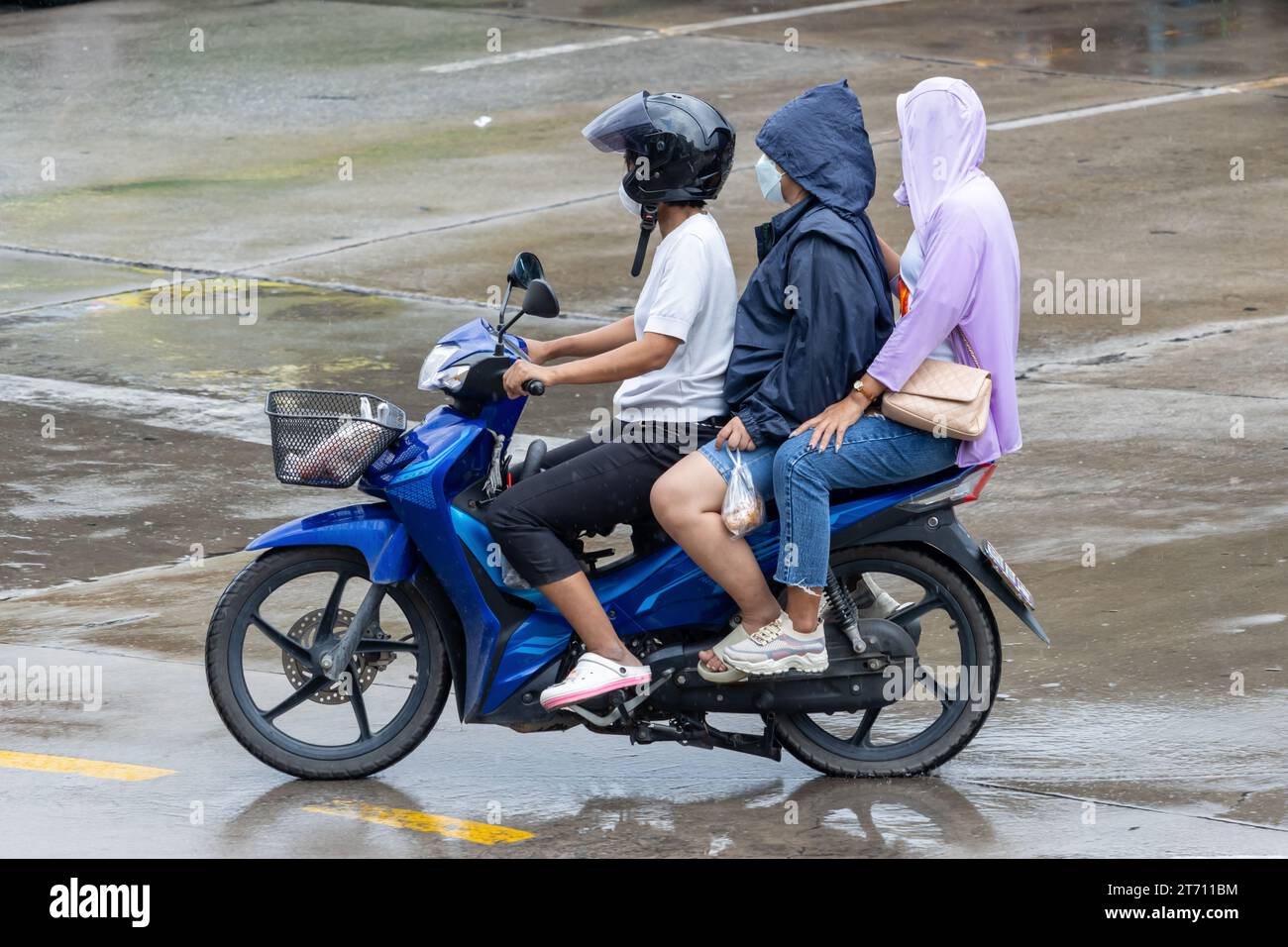 Un trio di donne cavalcano una moto sotto la pioggia, Thailandia Foto Stock