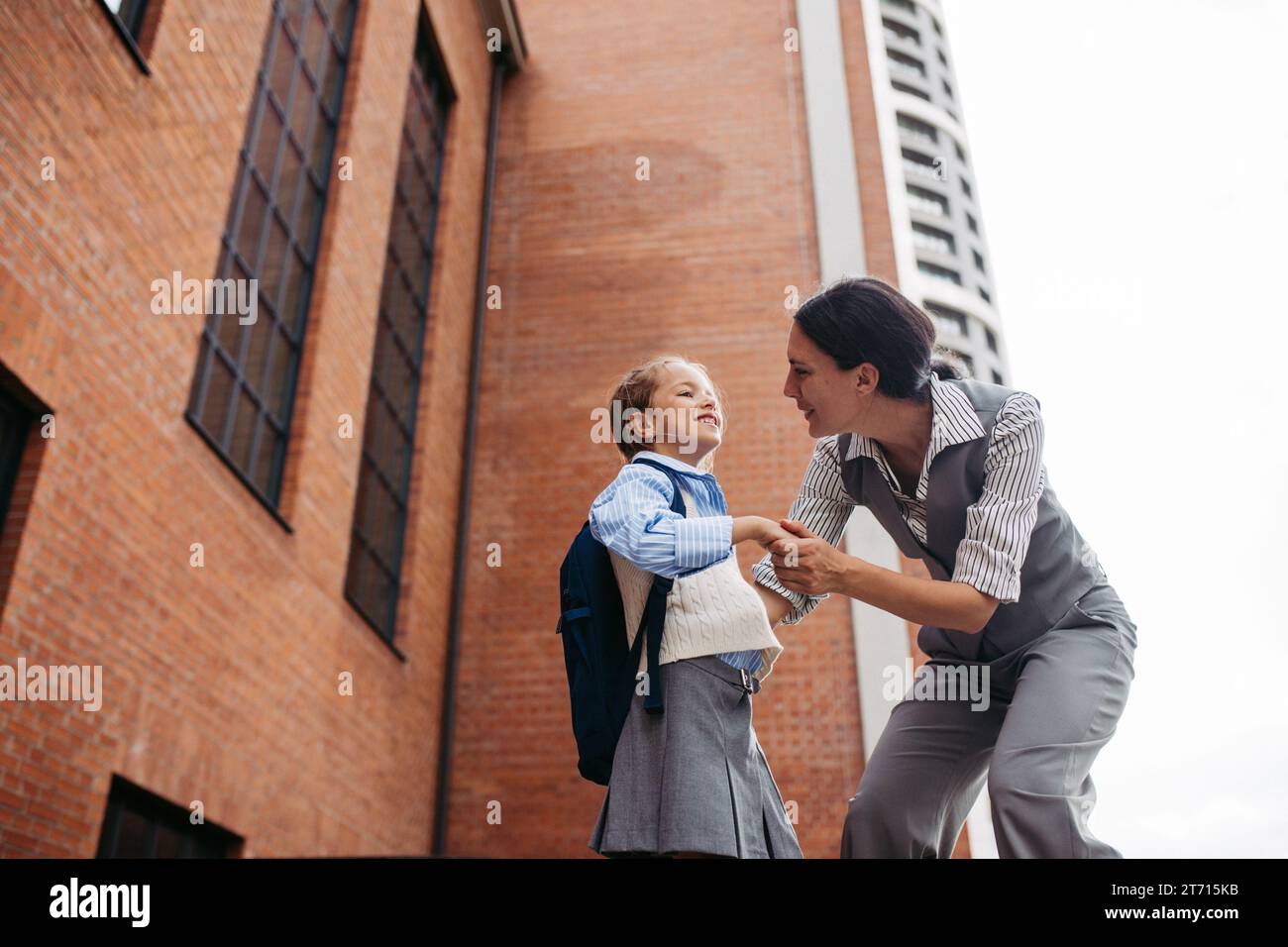 Madre lavoratrice che saluta la figlia davanti all'edificio scolastico e si dirige al lavoro. Concetto di equilibrio tra lavoro e vita privata per le donne. Foto Stock
