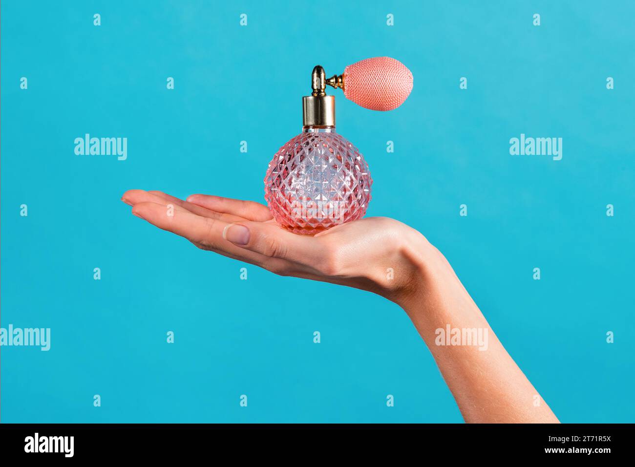 Anonimo sottile giovane donna che tiene la mano sul palmo profumo classico vintage con taglio a cristalli in flacone trasparente con spray atomizzatore a sacchetto di gas montato sulla parte superiore Foto Stock