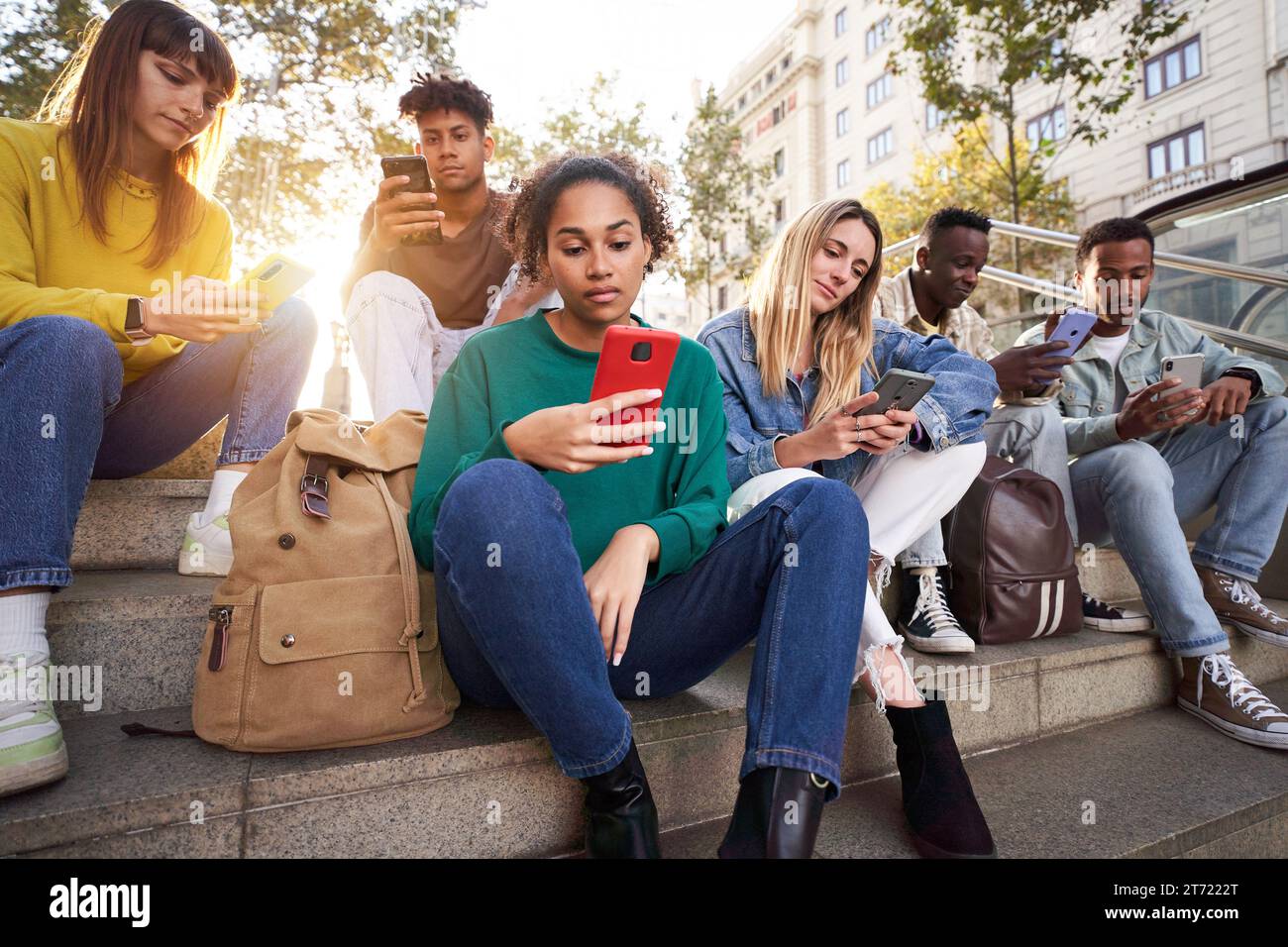Diversi gruppi di amici universitari seduti sulle scale della strada, studenti seri che usano il telefono. Foto Stock