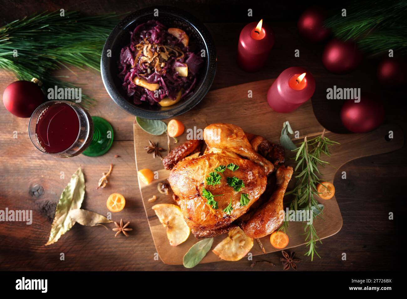 Pollo arrosto con cavolo rosso e vino su legno rustico scuro con candele e decorazioni natalizie, cena a base di pollame per le festività, vista dall'alto Foto Stock