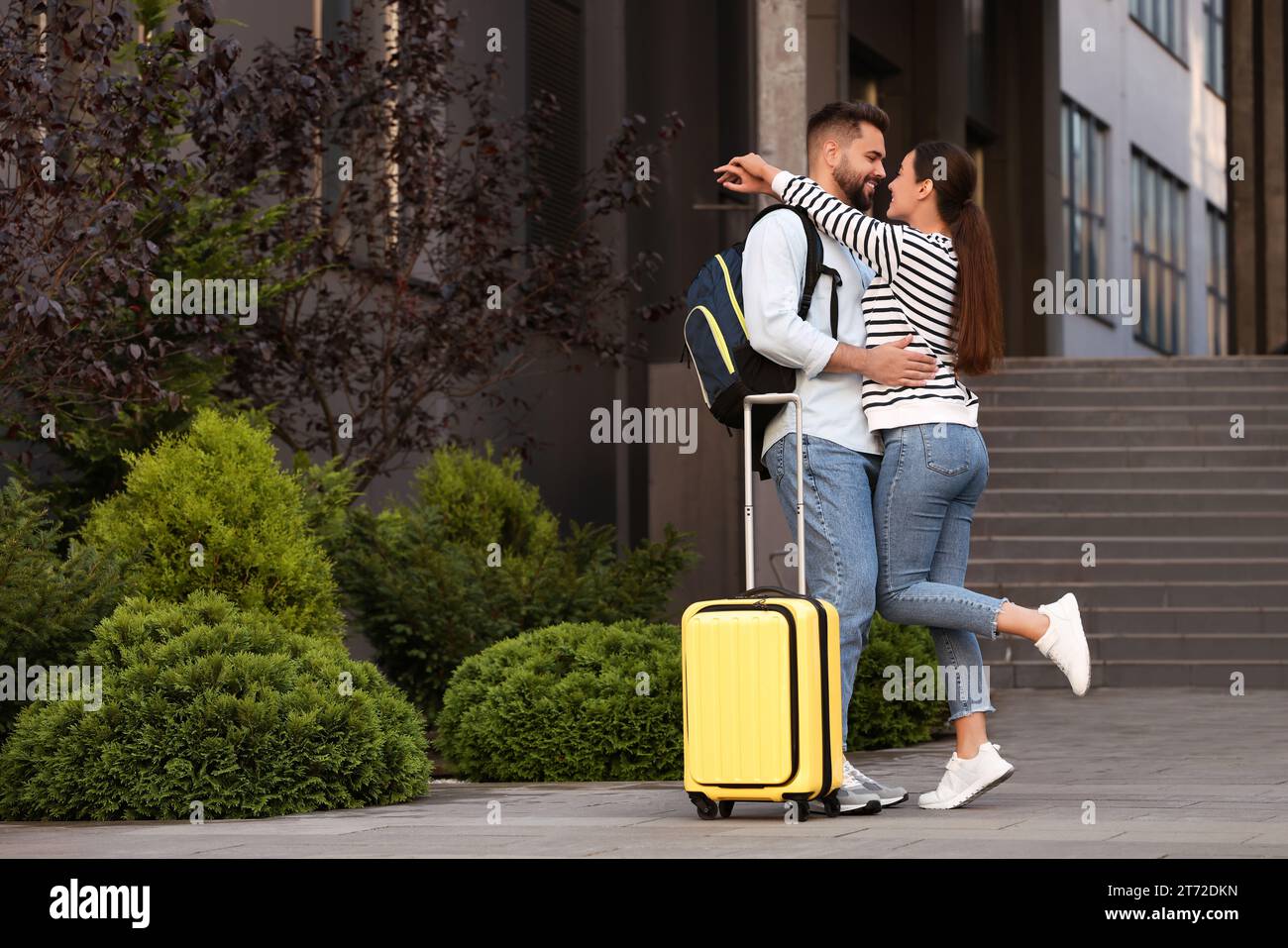 Relazione a distanza. Bella coppia giovane con bagagli che si abbracciano vicino all'edificio all'aperto Foto Stock