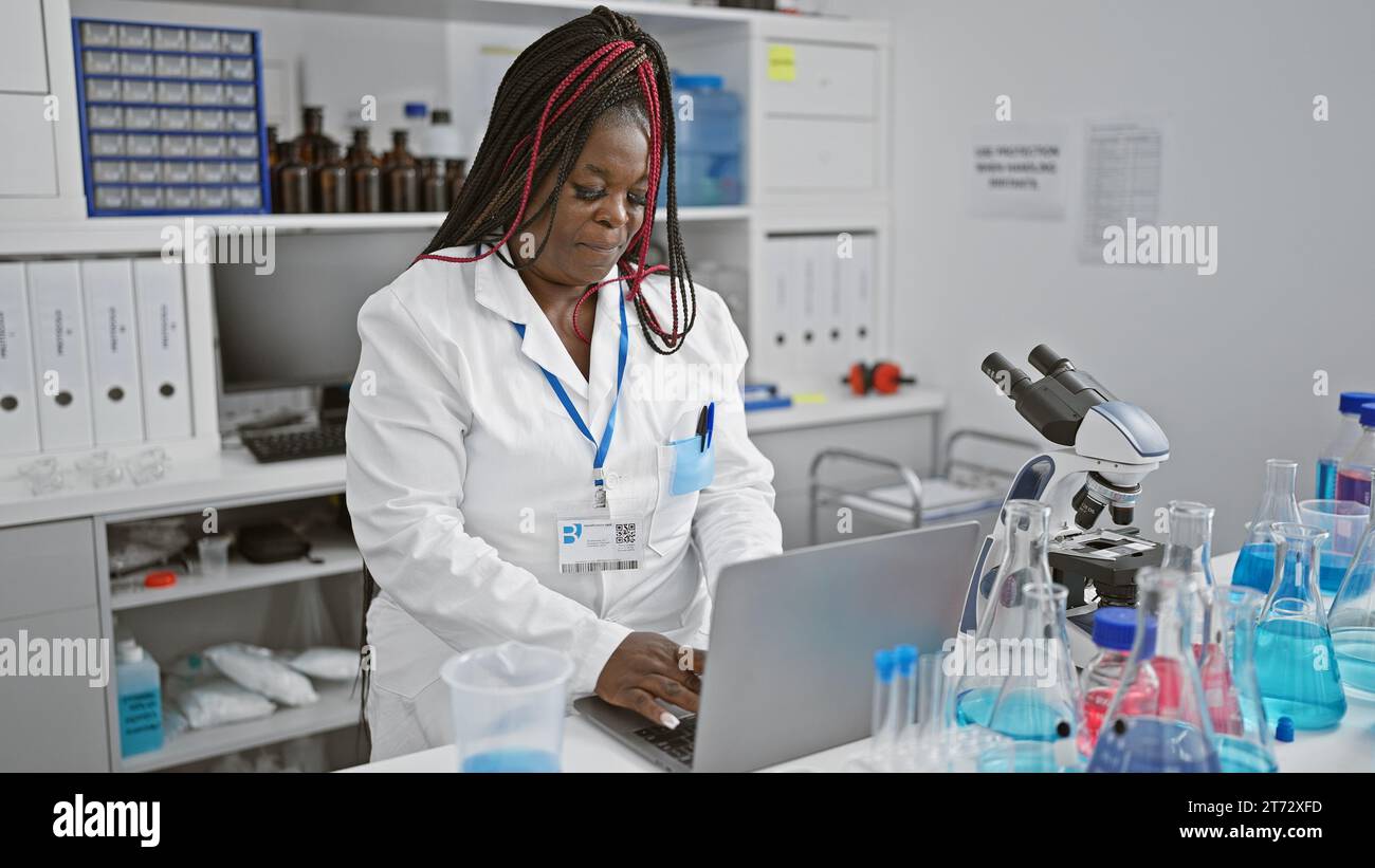 Scienziata afroamericana concentrata impegnata in una seria ricerca medica sul suo portatile in laboratorio, ritratto di un bellissimo adulto con trecce consegnare Foto Stock