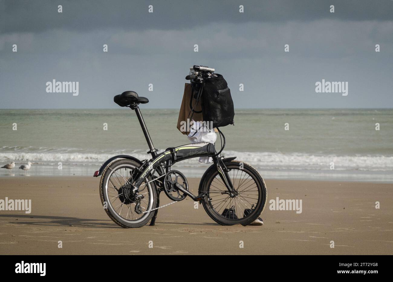 Bicicletta bilanciata su un banco, su una spiaggia di sabbia vuota, con due gabbiani e un paio di scarpe da ginnastica. Carrero Crosscity, E.. Foto Stock