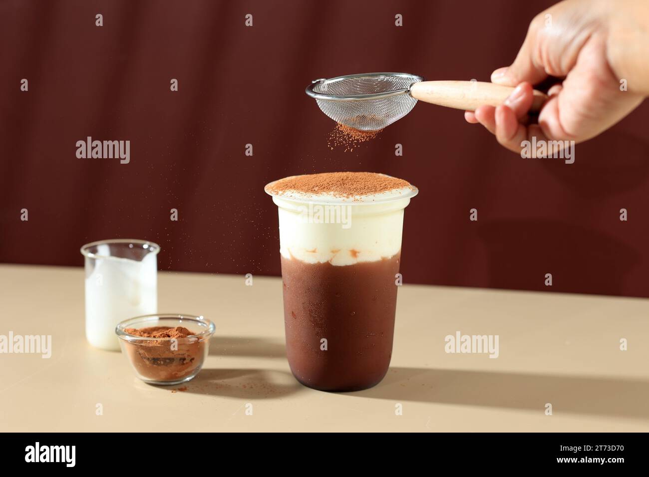 Mani versando la polvere di cacao alla bevanda con crema di latte al cioccolato, bevanda asiatica, spazio per i testi Foto Stock