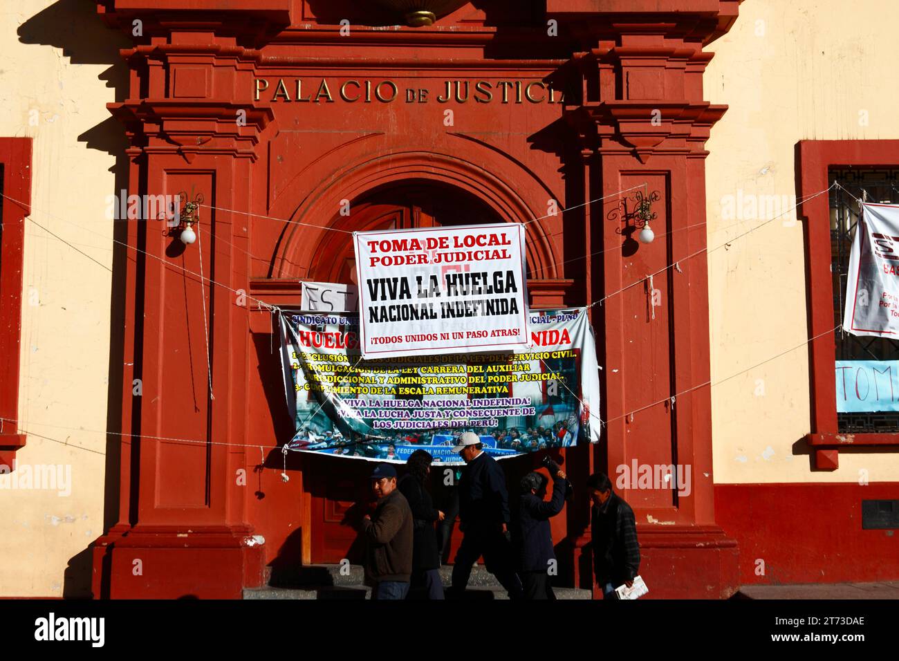 La gente passa accanto ai cartelli all'ingresso del Palacio de Justicia / Palazzo di giustizia che annunciano uno sciopero indefinito da parte dei lavoratori, che hanno rilevato l'edificio. Plaza de Armas, Puno, Perù. La disputa riguardava l'inclusione dei lavoratori della giustizia in una nuova legge per i lavoratori del servizio pubblico (che, a loro avviso, minaccia l'autonomia del sistema giuridico), e anche modifiche al sistema retributivo. Foto Stock