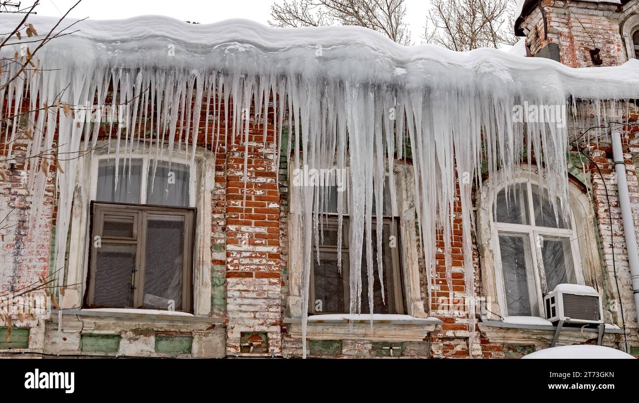 Enormi ghiaccioli affilati pendono pericolosamente dal tetto di una vecchia casa. Foto Stock