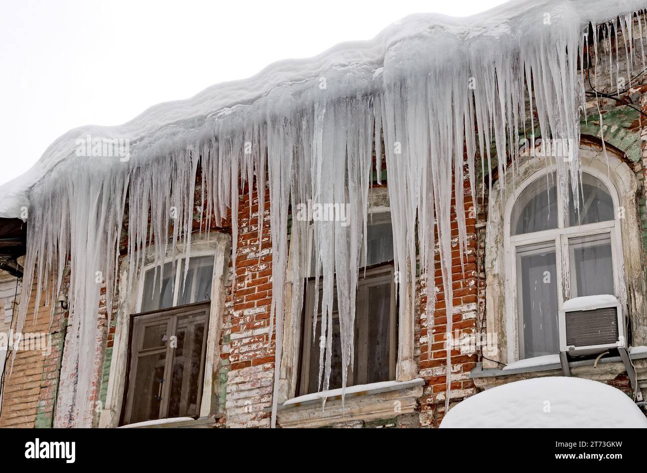 Enormi ghiaccioli affilati pendono pericolosamente dal tetto di una vecchia casa. Foto Stock