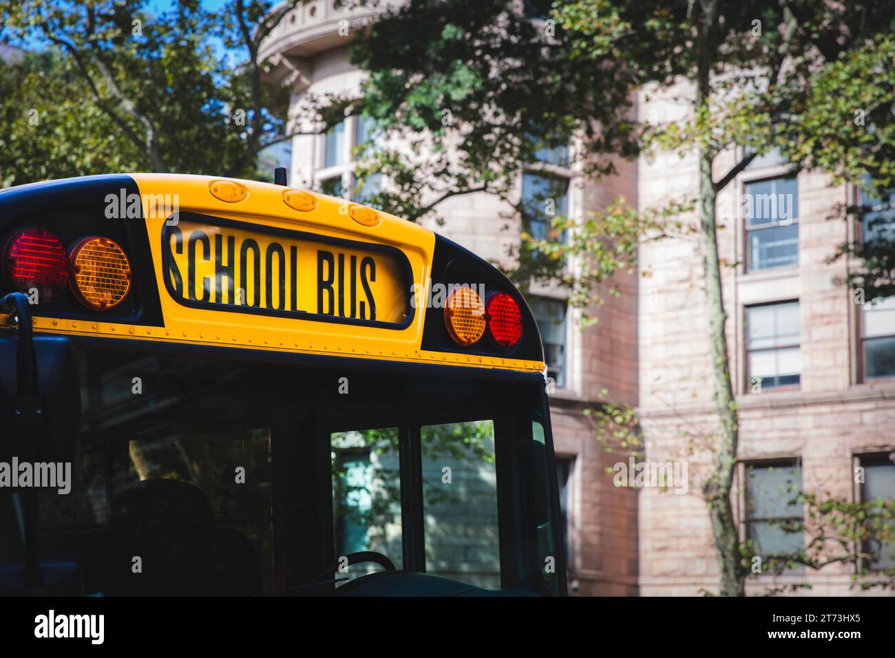 Un primo piano del fronte di un tradizionale scuolabus giallo americano con grandi insegne e luci di sicurezza in un ambiente cittadino Foto Stock
