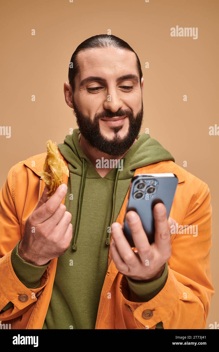 uomo felice con baklava e smartphone sullo sfondo beige, dessert tradizionale medio orientale Foto Stock