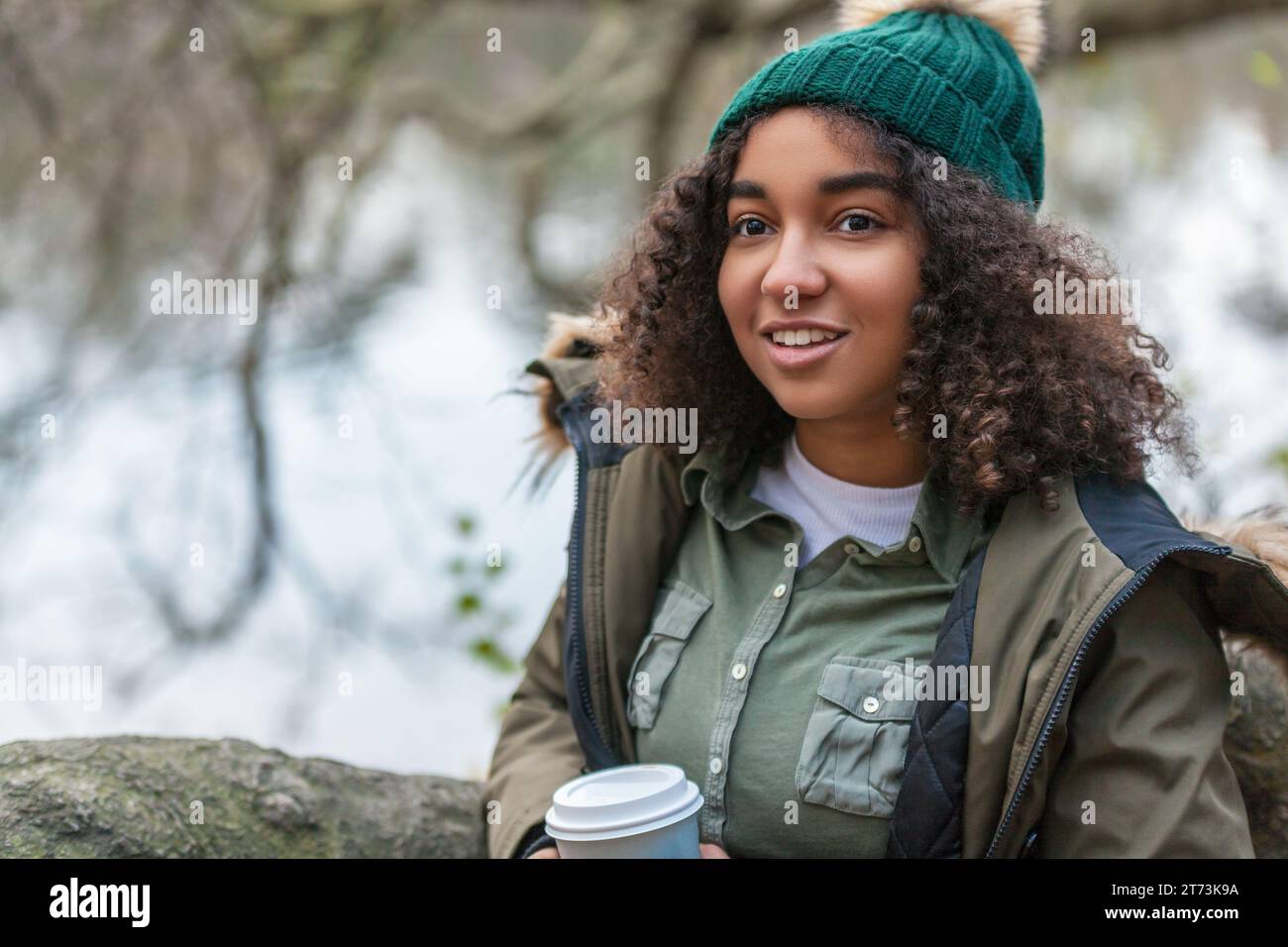 Bella allegra razza mista birazziale afroamericana adolescente donna che sorride bevendo caffè da asporto fuori indossando berretto cappello e.. Foto Stock