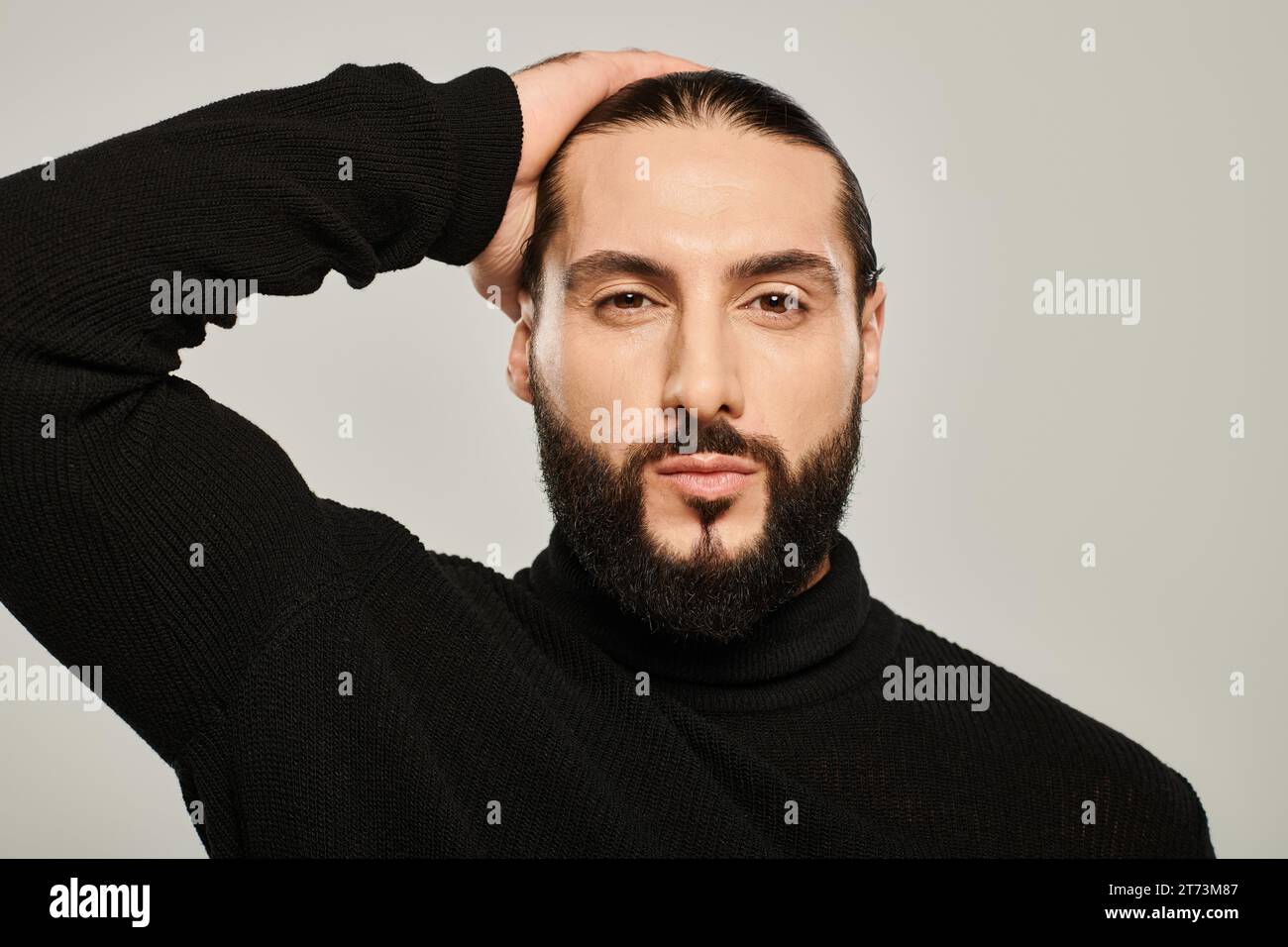 bellissimo uomo mediorientale con dolcevita nera, con sfondo grigio, ben vestito e curato Foto Stock