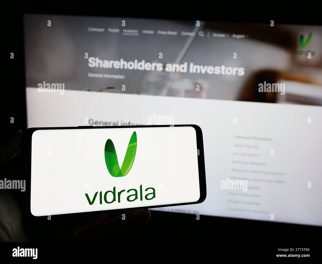 Persona in possesso di un cellulare con il logo della società spagnola di produzione del vetro Vidrala S.A. davanti alla pagina web aziendale. Concentrarsi sul display del telefono. Foto Stock